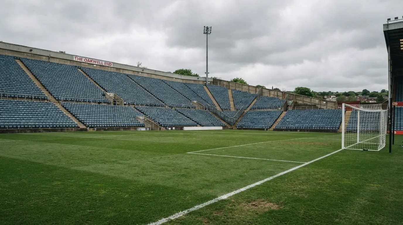 Rzędy pustych plastikowych krzesełek małego stadionu widziane z poziomu murawy pod pochmurnym niebem.