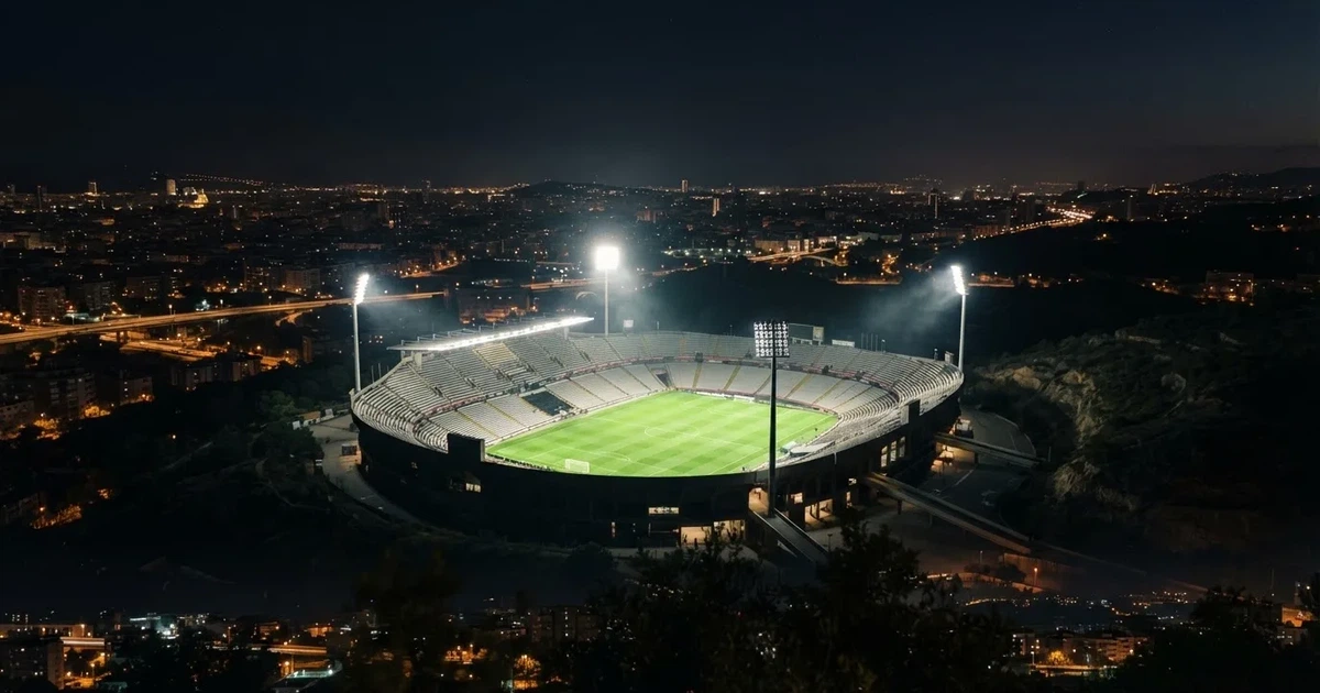 Stadion piłkarski nocą widziany z dużej odległości, jasne reflektory nad murawą i ciemne niebo wokół.