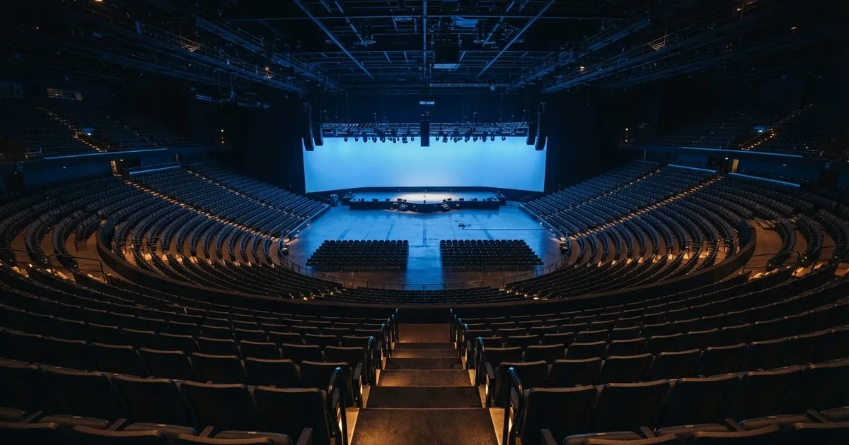 Pusta arena z półkolem siedzisk i oświetloną niebieskim światłem sceną, widok z góry na rzędy foteli.