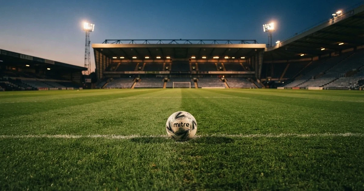 Piłka nożna leży na środku świeżo skoszonej murawy, w tle pusty stadion w świetle reflektorów wczesnym wieczorem.
